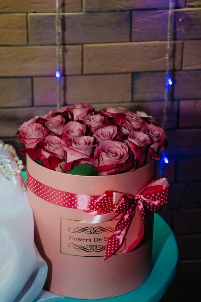 Charming pink roses arranged in a decorative gift box with ribbon, set against a warm backdrop.